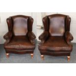 A Pair of Reproduction Wing-Back Armchairs, upholstered in brown close-nailed leather, on beech