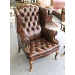 Canella: A Reproduction Wing-Back Chair, upholstered in brown buttoned and close-nailed leather,