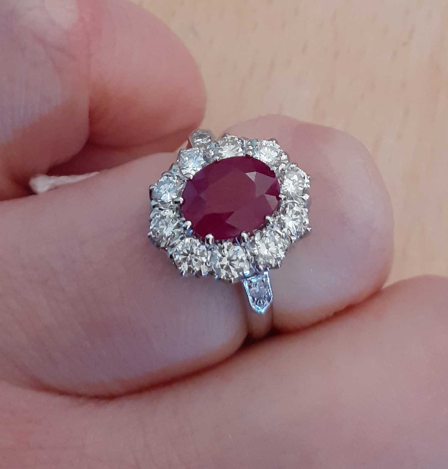 A Ruby and Diamond Cluster Ringthe oval cut ruby within a border of round brilliant cut diamonds, in - Image 2 of 4