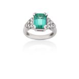 An Emerald and Diamond Ringthe emerald-cut emerald in a white claw setting, to round brilliant cut