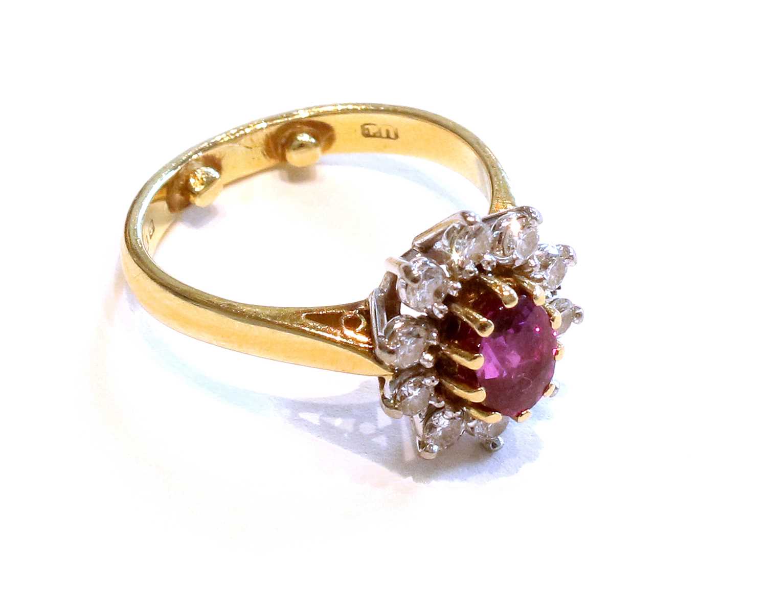 An 18 Carat Gold Ruby and Diamond Cluster Ring, the oval cut ruby in a yellow claw setting, within a