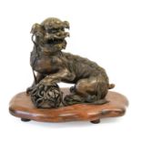 A Chinese Bronze Dog of Fo, Qing Dynasty, cast seated, a forepaw on a brocade ball, on a hardwood