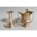 An American Silver Three-Handled Cup and an American Silver Chamber-Candlestick, the cup by