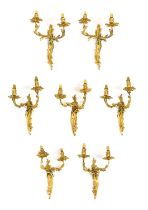 A Set of Seven Gilt Metal Twin-Light Wall Sconces, in Louis XV style, with leaf-sheathed sockets and