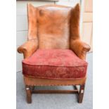 A George III Style Wing Back Armchair, upholstered in tan leather with brass studs and on mahogany