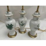 A Set of Three Porcelain and Parcel Gilt Table Lamps, decorated with green floral sprays, with