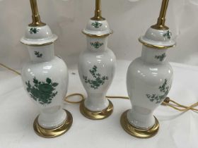 A Set of Three Porcelain and Parcel Gilt Table Lamps, decorated with green floral sprays, with