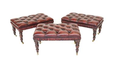 A Set of Three Buttoned Red Leather Footstools, with overstuffed seats, on Victorian-style turned