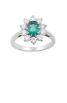 An 18 Carat White Gold Emerald and Diamond Cluster Ring the oval cut emerald within a border of