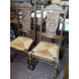 Pair of carved oak hall chairs with rush seats and carved profiles of a Breton man and woman