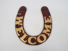 A cast iron, horseshoe shaped Welcome sign, approximately 30 cm x 27 cm,