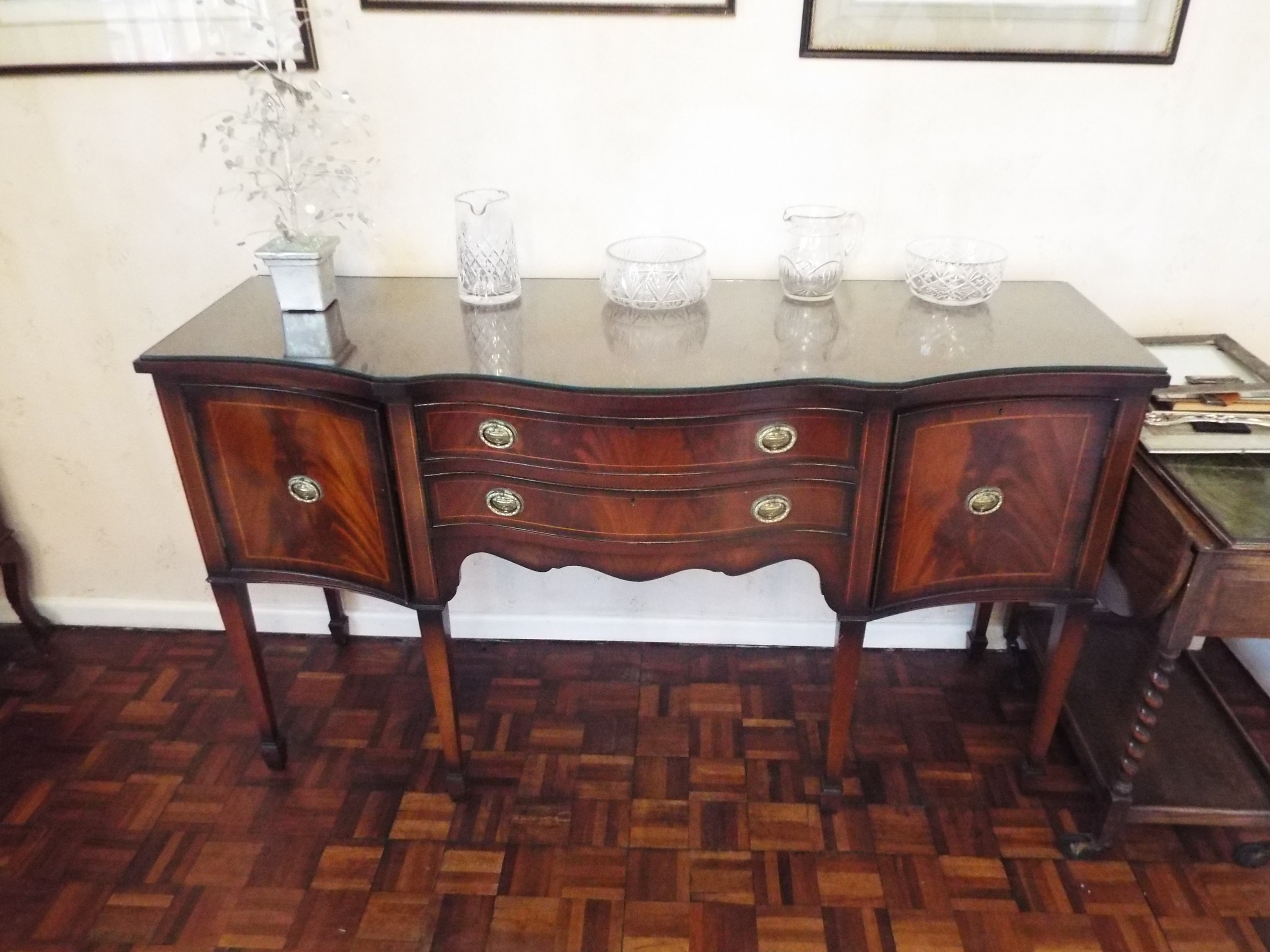 A sideboard having twin drawers flanked by single door cupboards with protective glass top,