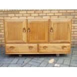 An Ercol Windsor sideboard with three cupboard doors over two drawers,