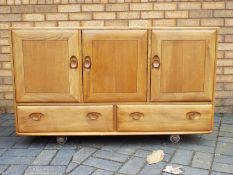 An Ercol Windsor sideboard with three cupboard doors over two drawers,