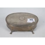 An Edwardian silver dressing table box of oval section raised on four paw supports,