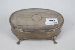 An Edwardian silver dressing table box of oval section raised on four paw supports,