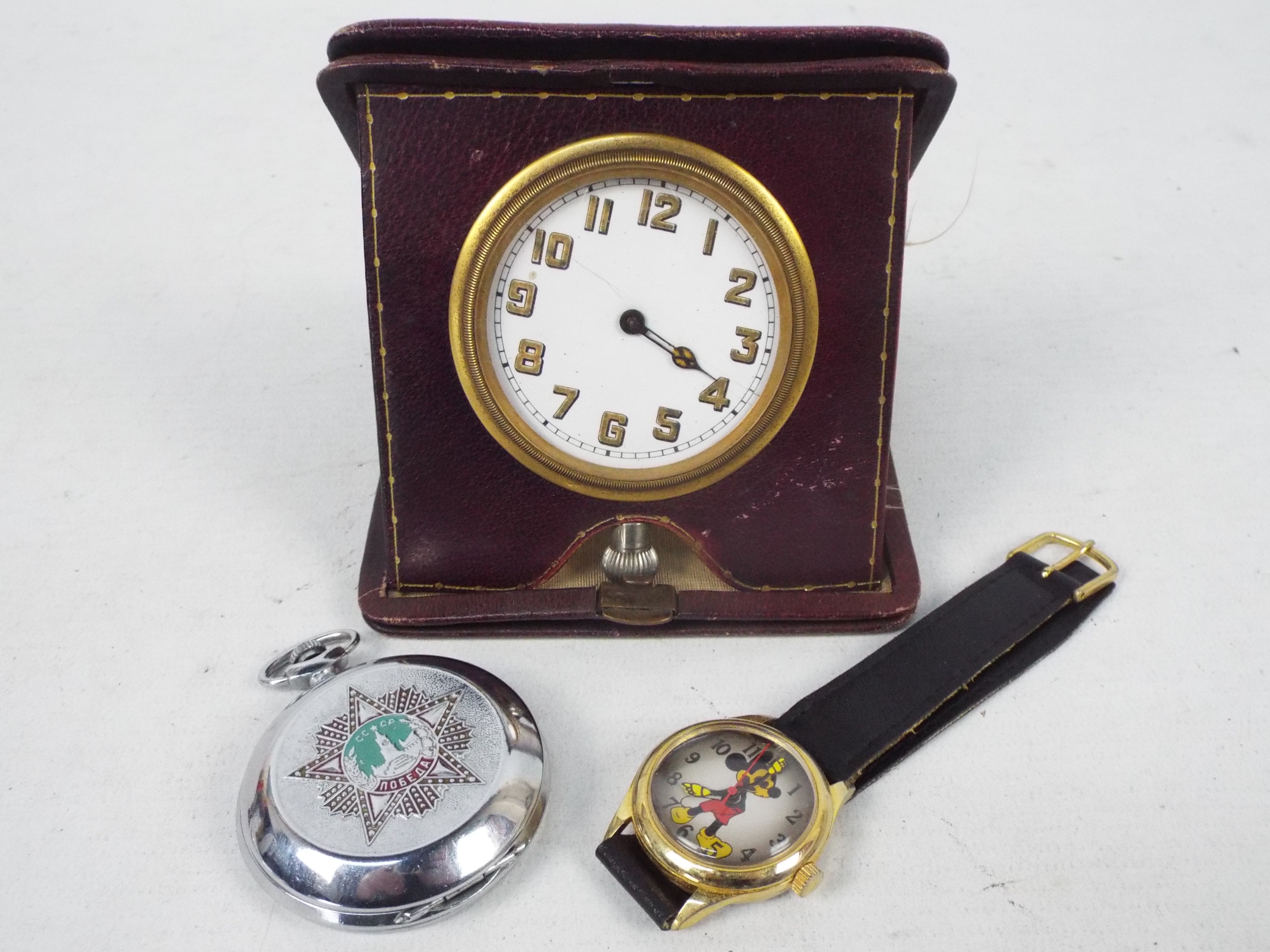 A vintage German travel clock in leather pouch, Russian pocket watch and a wrist watch.