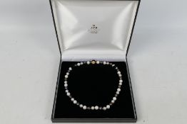 A pearl necklace compromising black, grey and white alternating pearls, each approximately 9 mm,