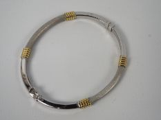 An 18ct gold two-tone hinged bangle with safety clasp, 5.
