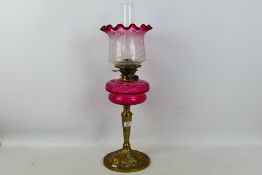 A brass oil lamp with cranberry glass font (font approximately 19 cm diameter) and cranberry tinted