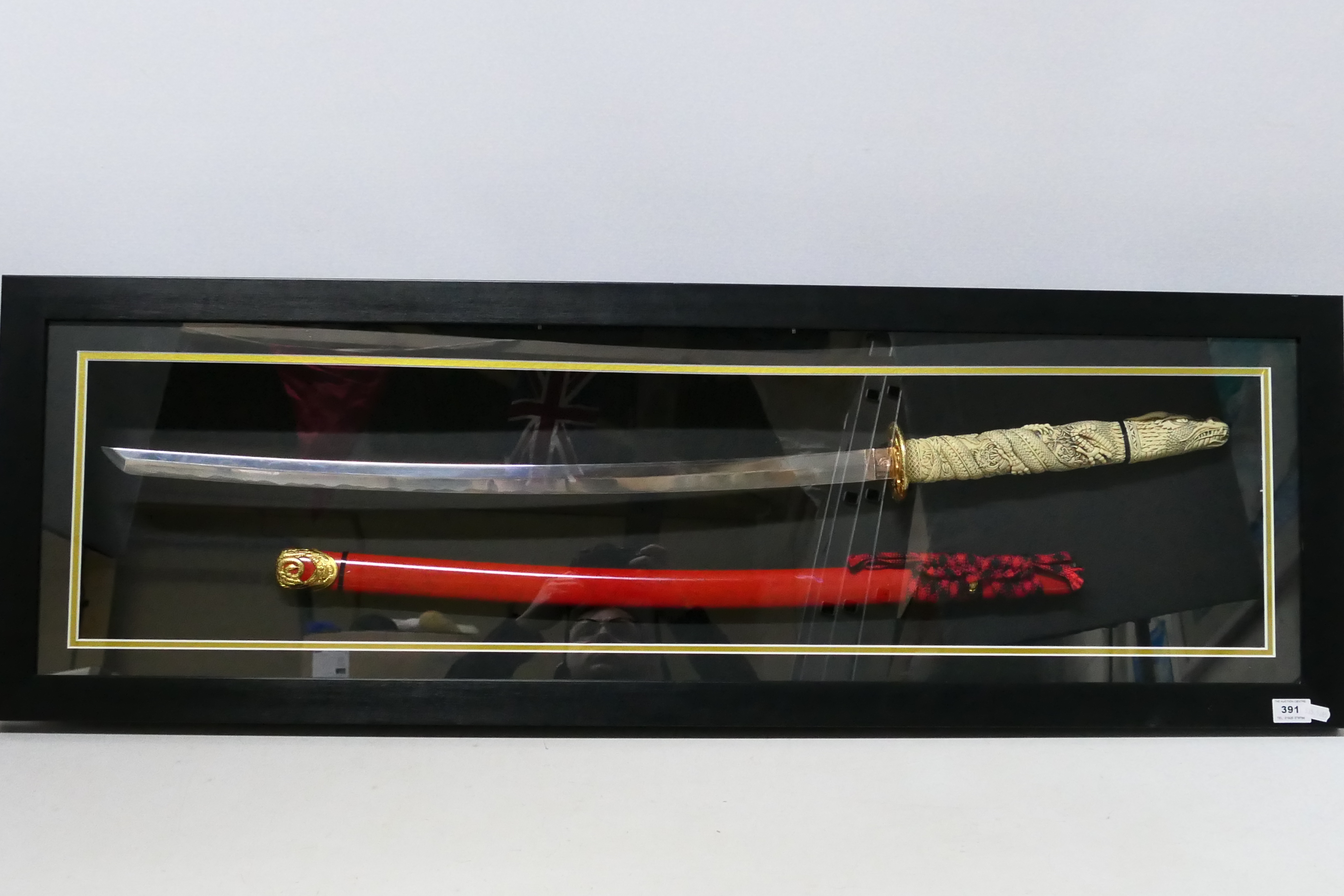 A decorative Japanese sword display comprising katana with dragon form hilt and red lacquered saya,