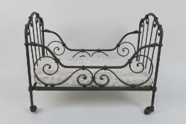 A Napoleon III doll's cot / day bed, iron framed and raised on castors,