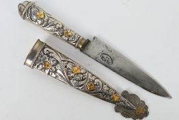 A white and gilt metal Argentinian Gaucho knife with floral decorated hilt and scabbard,