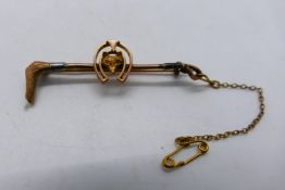 A rose metal bar brooch, stamped 9ct, in the form of a hunting crop with fox mask within horseshoe,