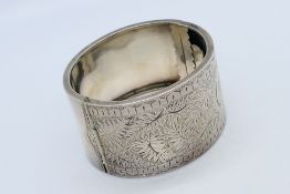 A white metal (presumed silver) bangle with inscribed foliate scrolls, approx 34.3 gm.