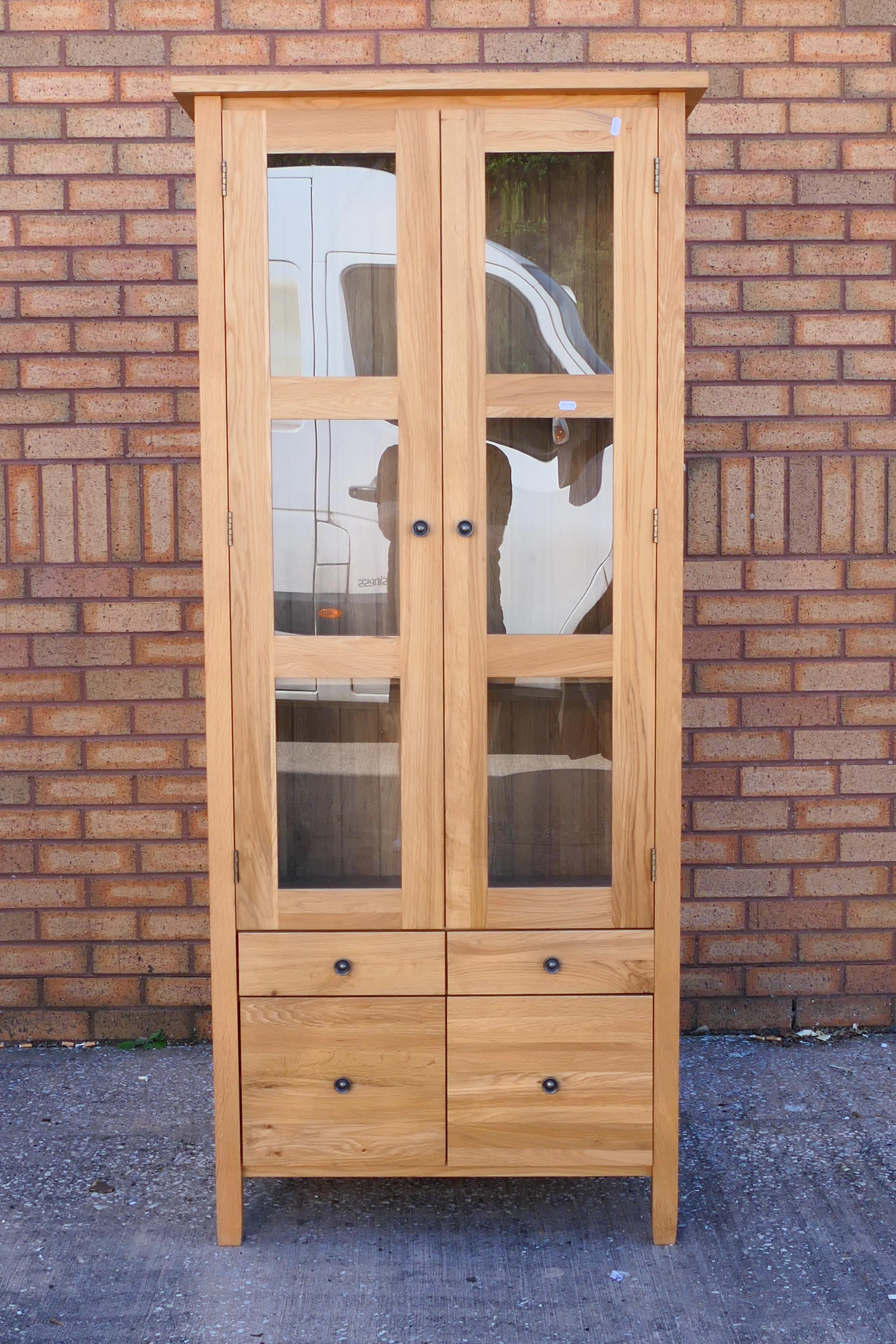 A light oak cabinet with twin glazed doors enclosing two shelves over four short drawers,