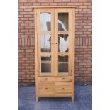 A light oak cabinet with twin glazed doors enclosing two shelves over four short drawers,