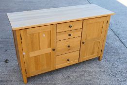 A light oak sideboard with four central, graduated drawers flanked by single door cupboards,