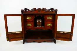 An early 20th century oak smokers cabinet with twin bevel glazed doors opening to reveal four