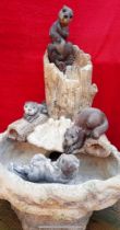 A Henri Studio composite stone water feature in the form of otters around a tree trunk,