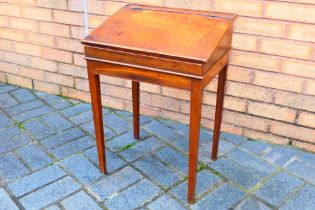 A vintage school desk with hinged top, raised on four tapering supports,