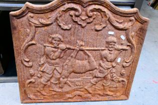 A vintage cast iron fireback depicting two men returning from hunting with their prey,
