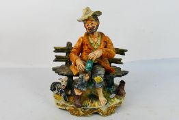 A capodimonte figure group depicting a man sat on a bench with a dog at his feet,