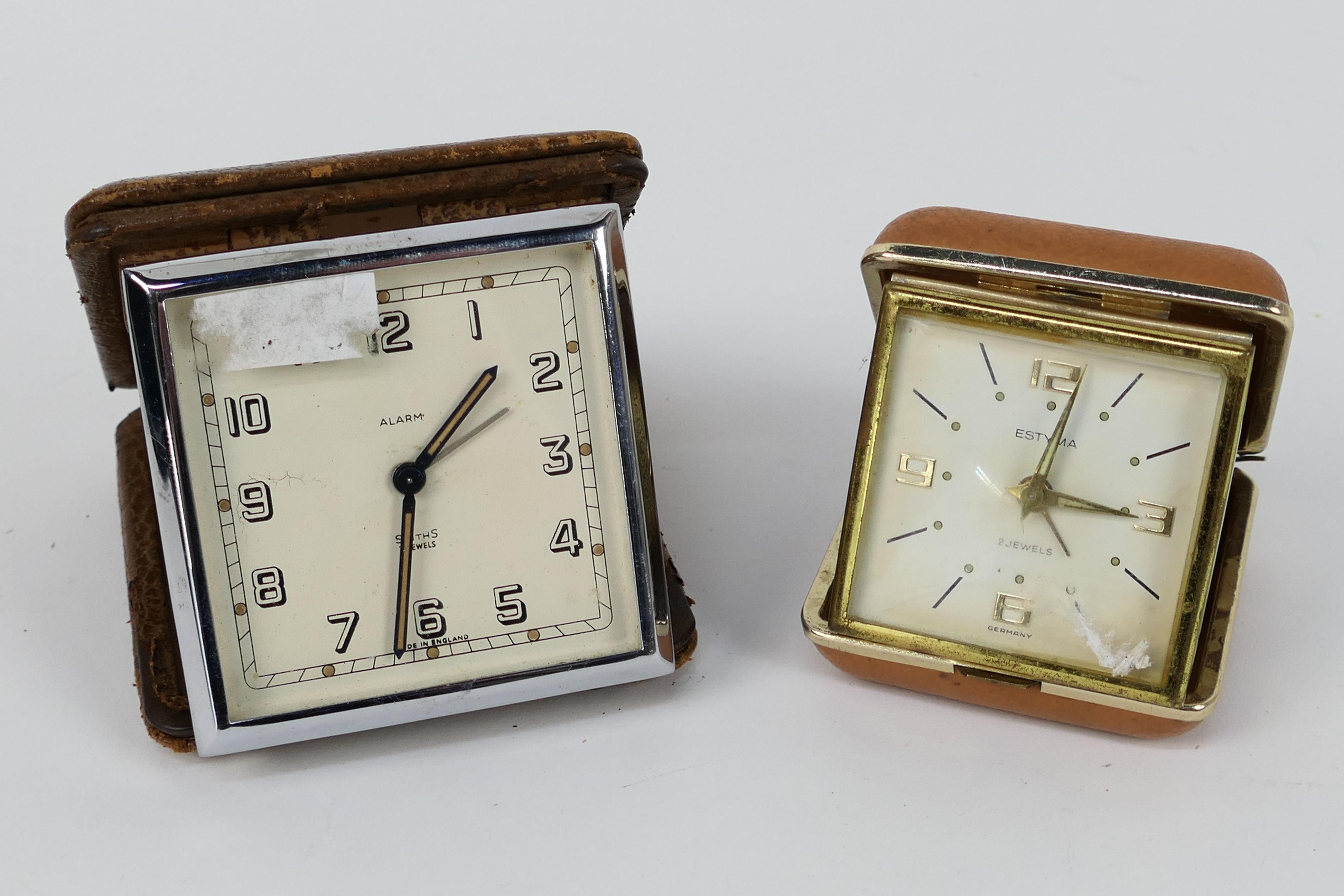 A Smiths Art Deco travel alarm clock in folding leather case, one further travel alarm clock.