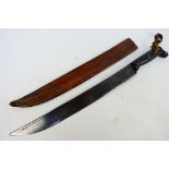 An antique machete with carved wooden grip and 45 cm (l) blade, contained in leather sheath,