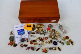 A polished wood box containing a quantity of enamelled pin badges and charms including several with