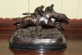 A large bronze model of steeplechasers jumping a brush fence on marble base, signed E.