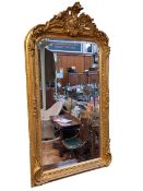 Rectangular gilt framed bevelled wall mirror with foliate decorated crest, 155cm by 84cm.
