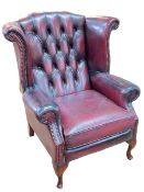 Ox blood leather button backed and brass studded wing armchair.