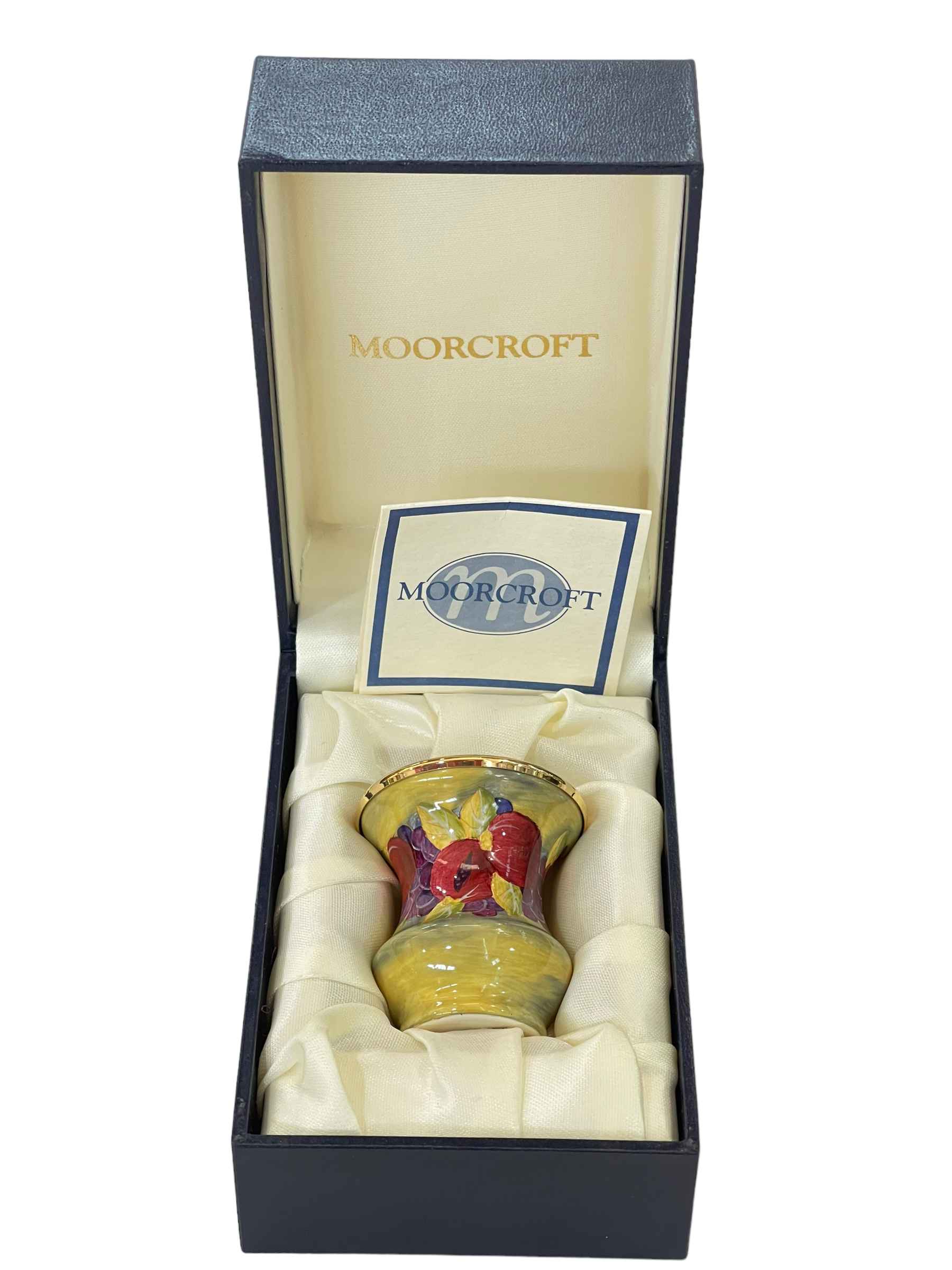Small Moorcroft enamel vase decorated with band of fruit on green ground, boxed.