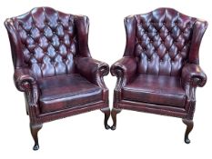 Pair ox blood button backed and brass studded wing armchairs.