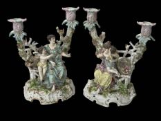Pair Continental porcelain candelabra featuring maidens and cherubs on garden bench with birds and