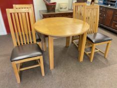 Circular light oak extending dining table with integral leaf and four rail back dining chairs.