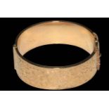 9 carat gold bangle, half engraved with scrolling foliage, 6.5cm across, boxed.