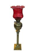 Vintage ornate brass columned oil lamp with red glass shade, 85cm.