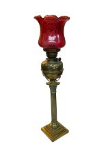 Vintage ornate brass columned oil lamp with red glass shade, 85cm.